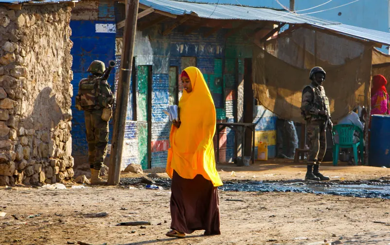 A woman walking past military men in Somalia.