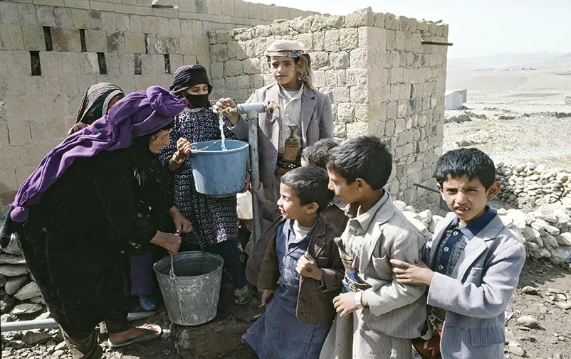 Kvinna och barn hämtar vatten från pump.