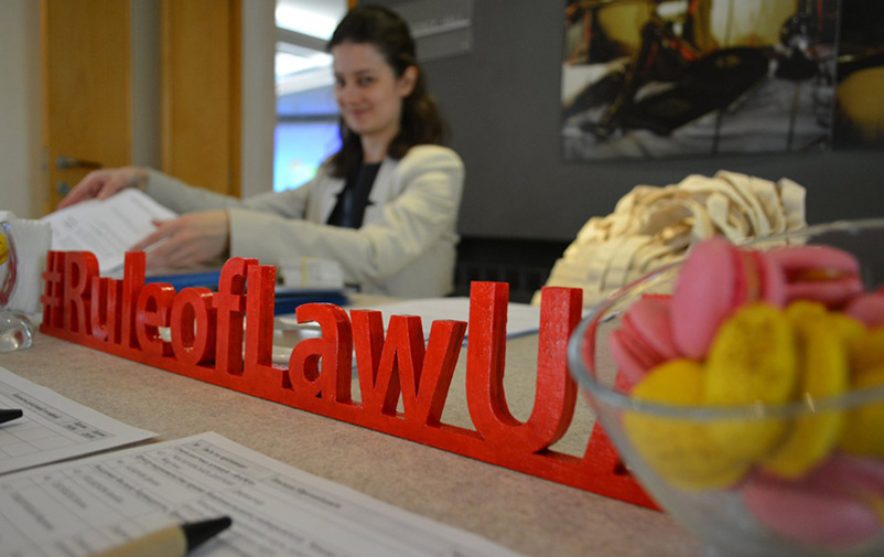 A woman behind a table who is out of focus. In the tables wooden letters saying Rule of Law in Ukraine.