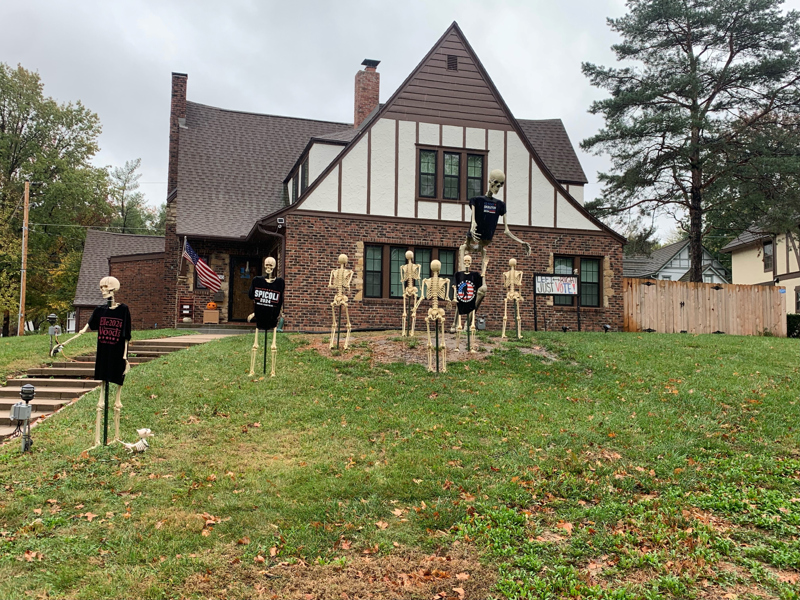 Halloweendekorationer i form av skelett i villaträdgård. Skylt som uppmanar till röstning.